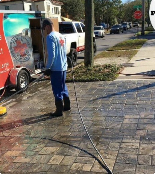 Pavers Rescue technician cleaning a brick paver driveway in Clearwater with a hose beside the branded service trailer