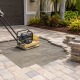 Contractor using plate compactor to repair lifted pool deck pavers in Tampa Bay FL area
