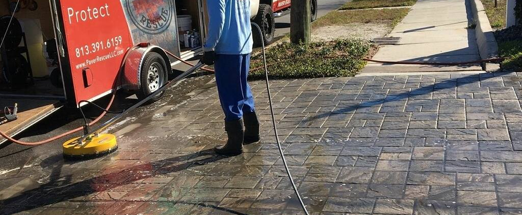 Paver Rescue technician pressure washing a brick paver driveway in Tampa FL with branded service trailer