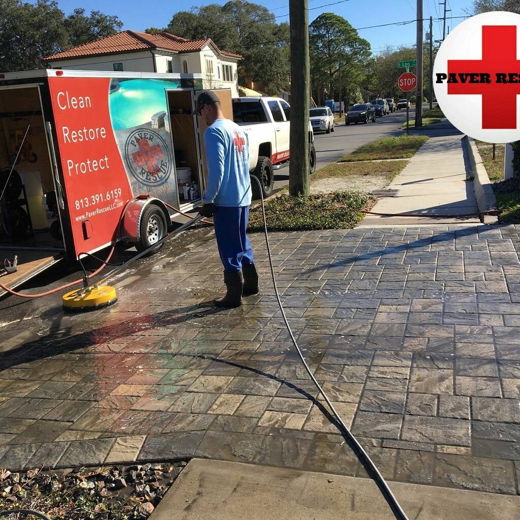 Paver Rescue technician pressure washing a brick paver driveway in Tampa FL with branded service trailer